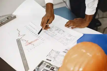 Manos de trabajadores revisando planos y documentos de construcción en una mesa de oficina