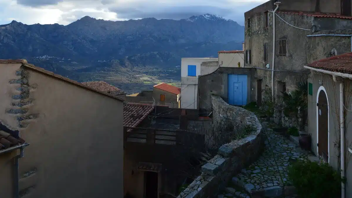 Pueblo de montaña con casas de piedra y tejados de teja, rodeado de picos nevados en la sierra