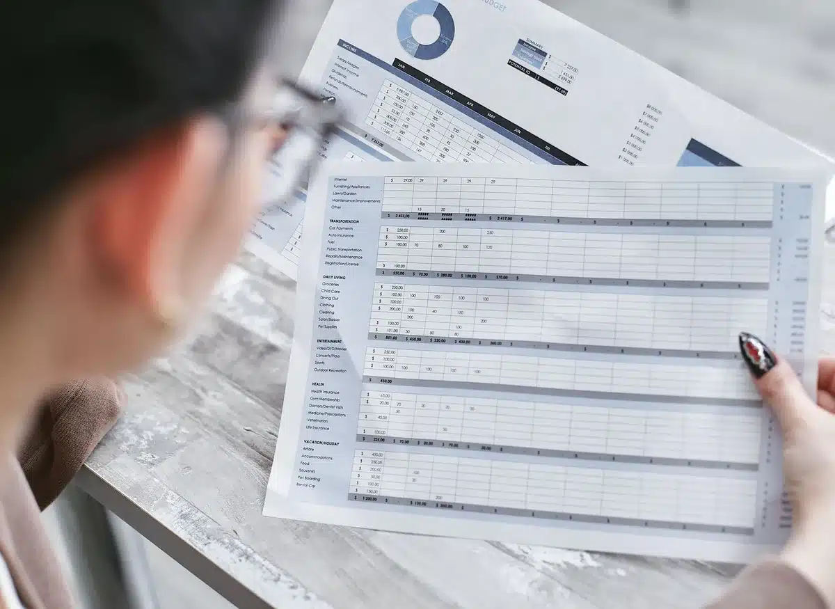 Persona revisando documentos financieros y comparando datos en una hoja de c&aacute;lculo