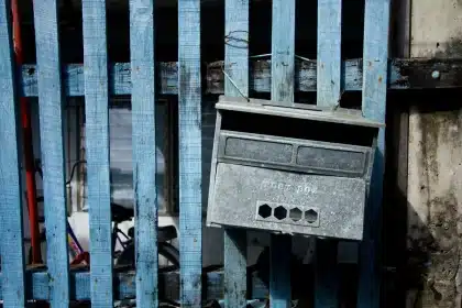 Trabajador postal clasificando y asegurando sobres de votación en un contenedor cerrado en almacén seguro