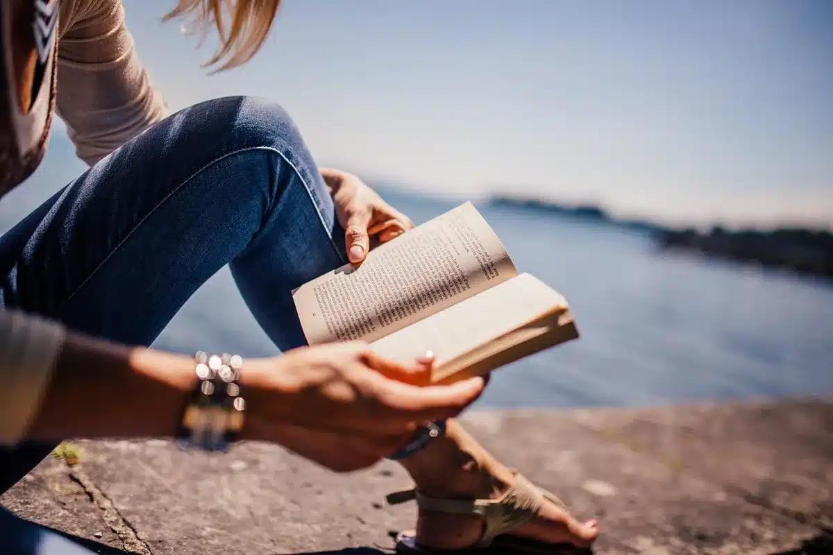 A simple scene of an open biography book on a wooden table with a pair of reading glasses and a pen nearby, hinting at research and portraiture