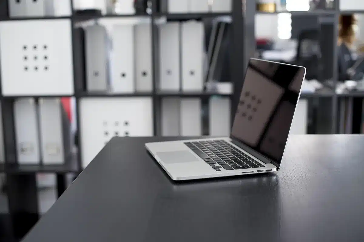 A minimalist workspace with an anonymous closed silver laptop on a wooden desk, a plain notebook and a pen beside it, soft daylight from a window, no logos or brands