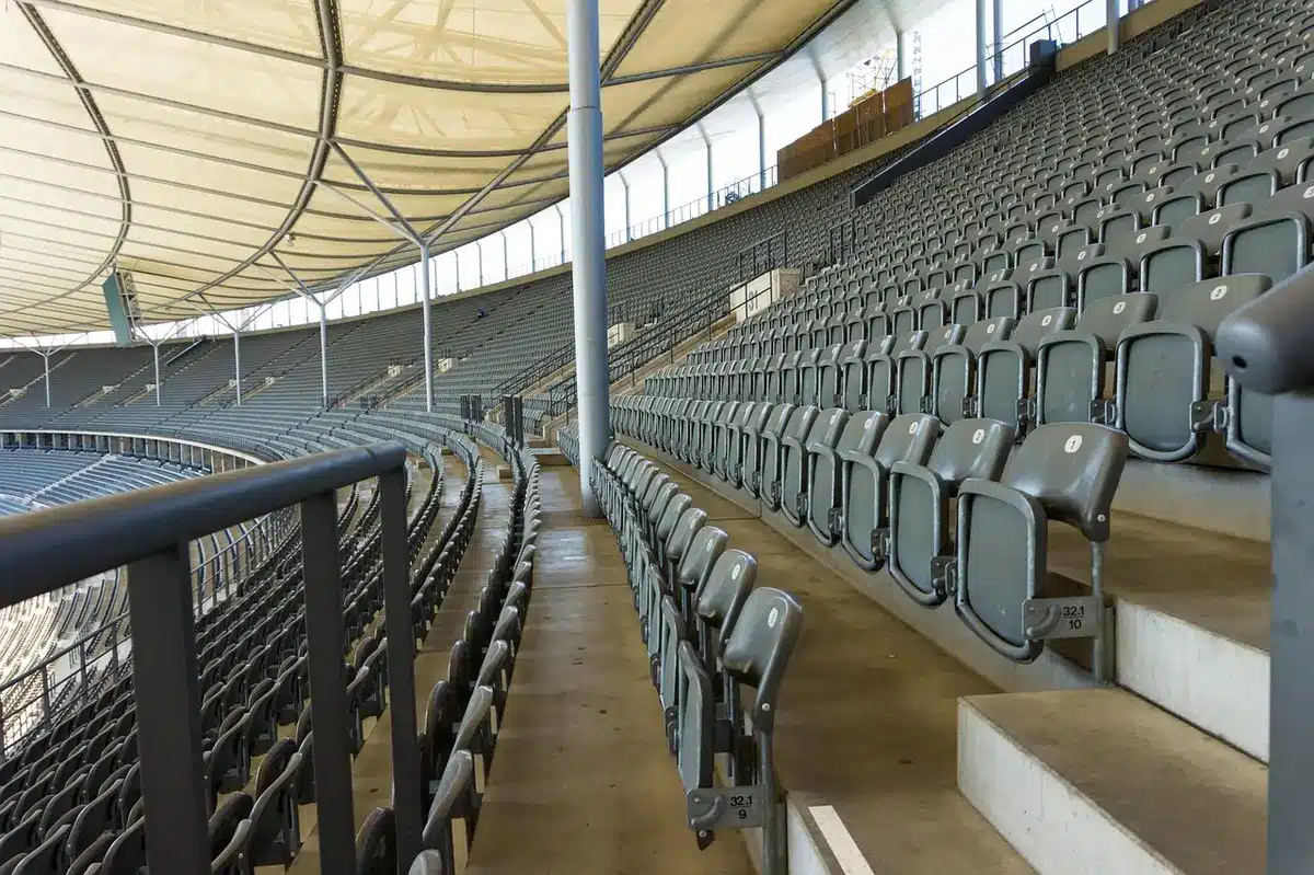 Empty home stadium with few scattered fans and a dim scoreboard showing a tied score