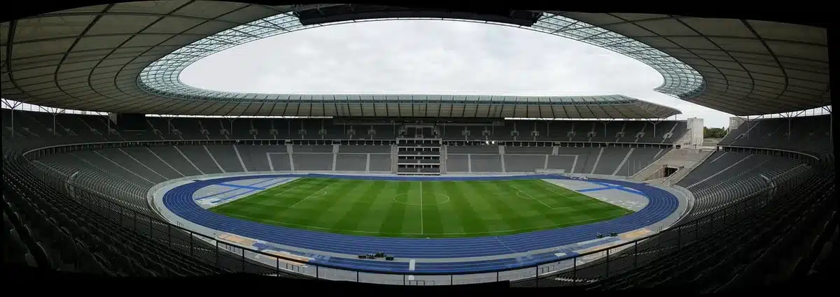 Empty, modular stadium interior with folded seating and team banners removed, anonymous cleaning staff preparing the pitch