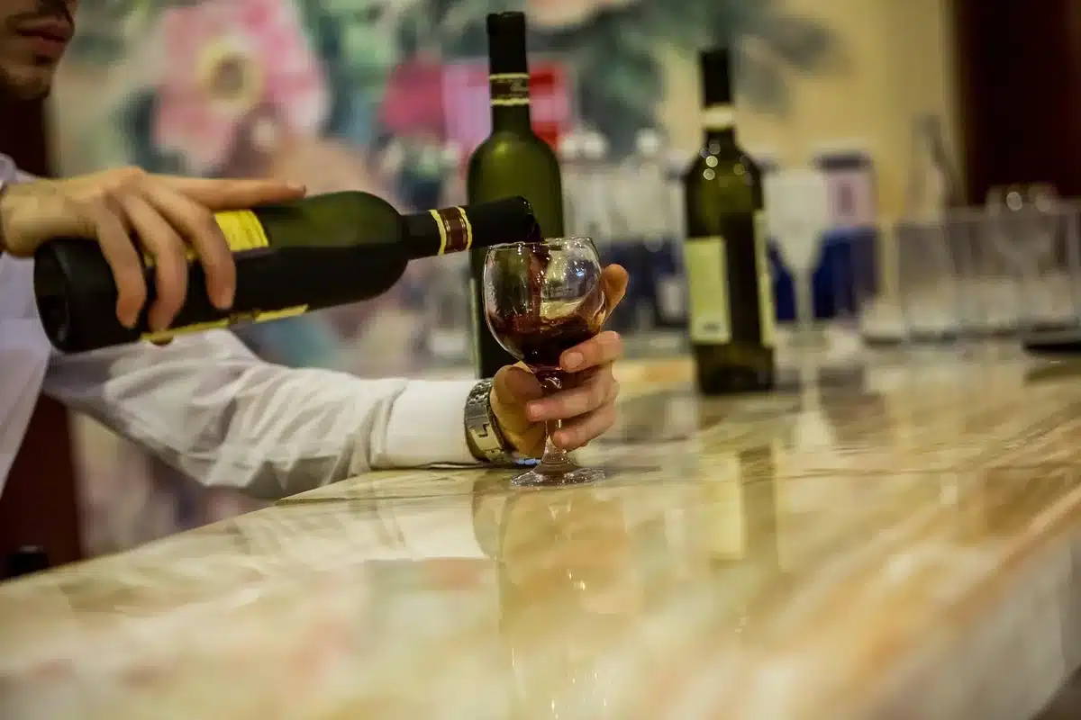 Interior of a small unbranded wine bar with wooden shelves of bottles and a single anonymous patron silhouette at the bar