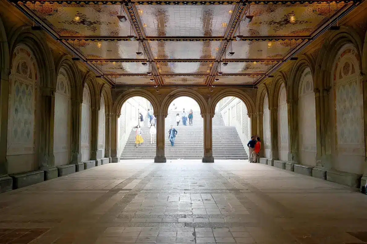 A low, arched brick tunnel entrance lit from within, empty pathway leading into shadow with historic stone walls and informational signage at the mouth