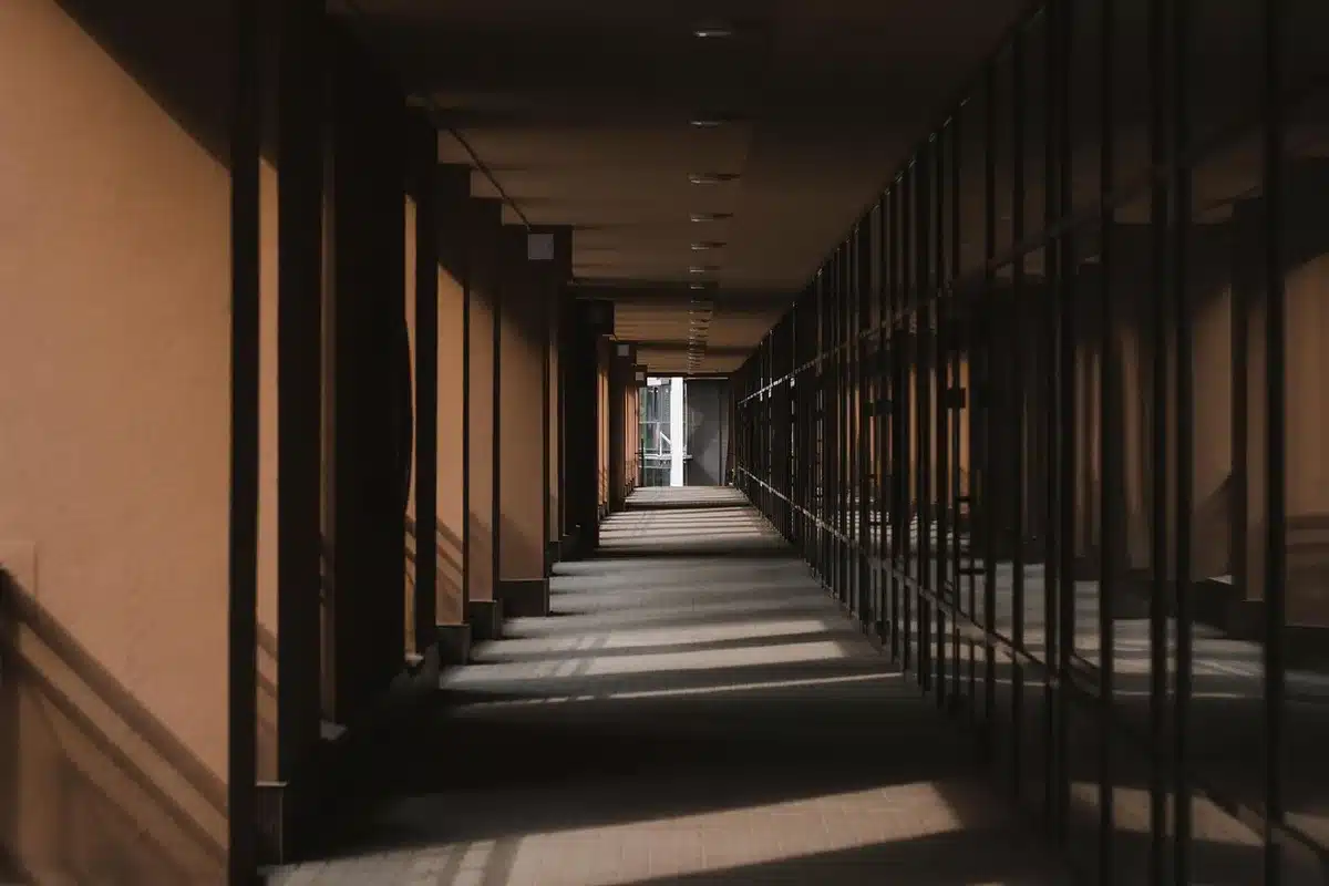 Interior view down a low vaulted corridor with old brickwork and faint rail traces on the floor; distant daylight at the far end, no people