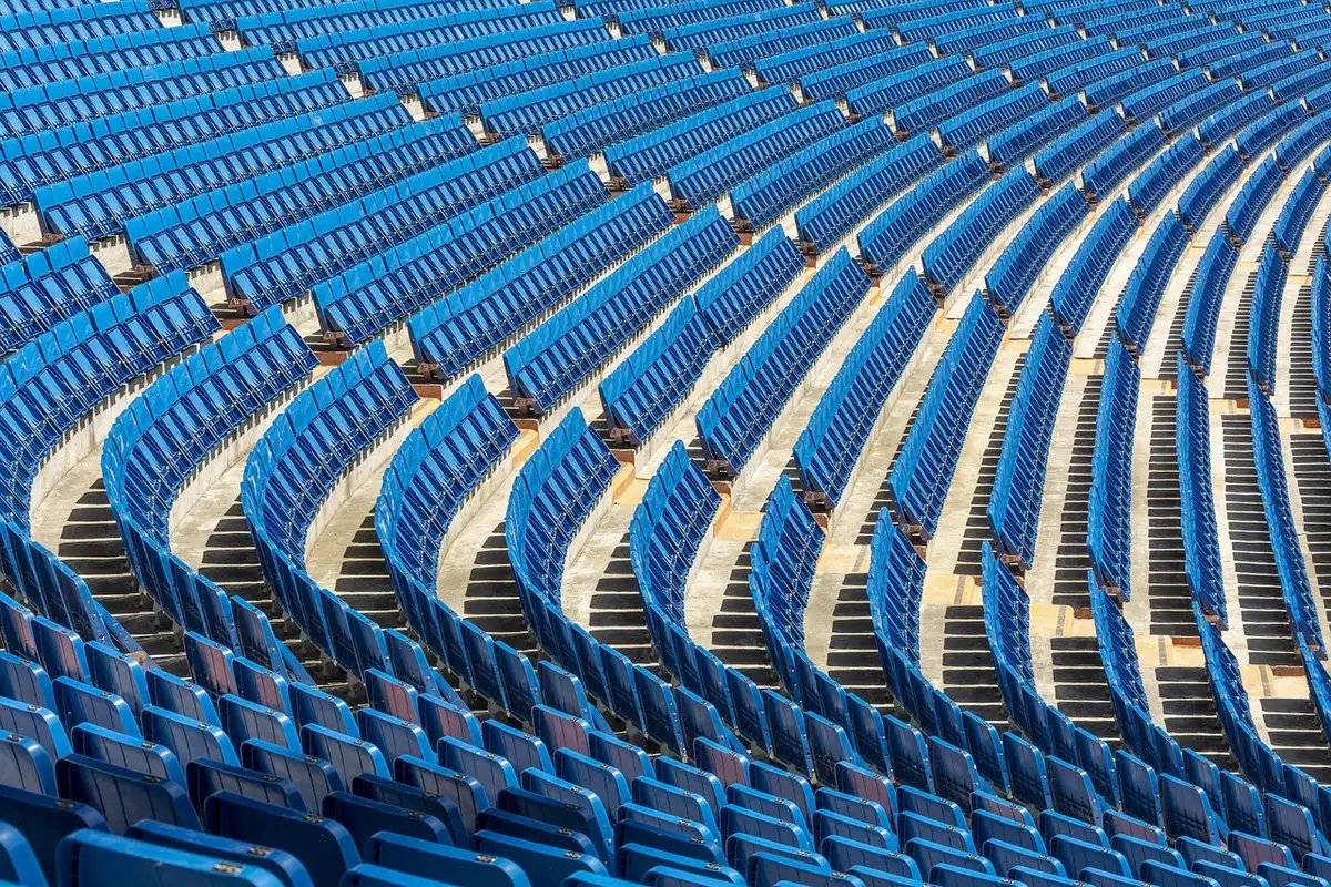 Anonymous small group of fans leaving a stadium under floodlights, scarves blurred, empty pitch in background