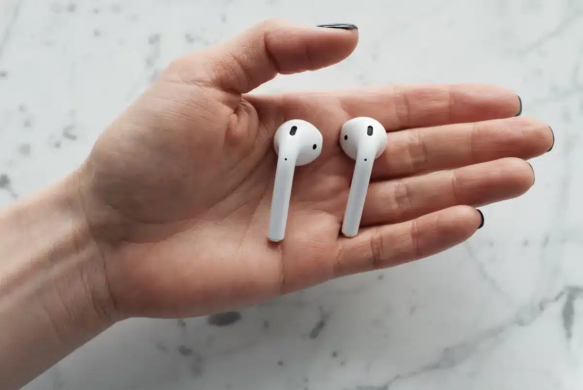 Close-up of a generic white wireless earbud and its charging case placed on a plain counter with a small printed price tag next to it