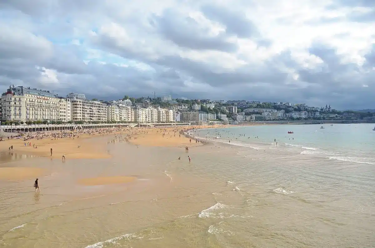 A wide empty beach promenade under a cloudy sky with distant rain squalls approaching the coastline; no people in close view, moody low clouds over Mediterranean water