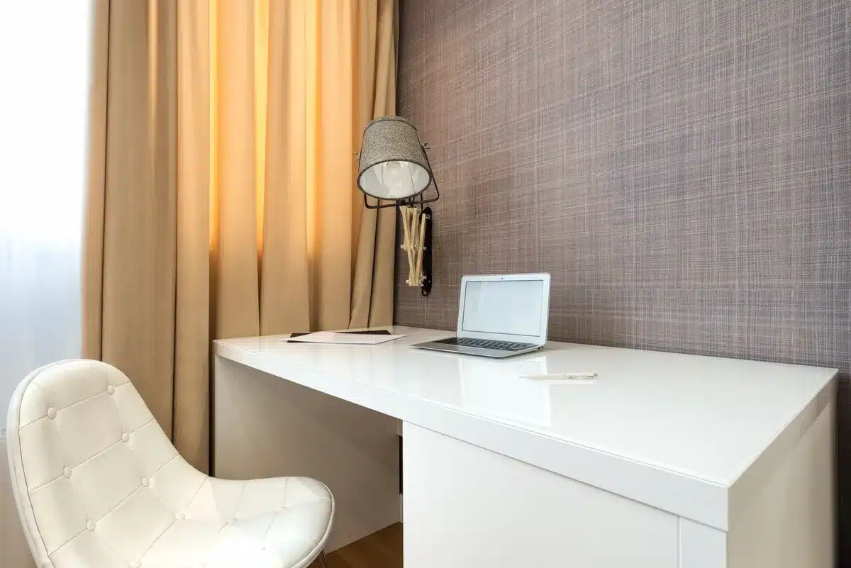 Wide interior shot of an empty, anonymous home office with a closed laptop on a desk and a dim lamp; scene suggests data/privacy at stake