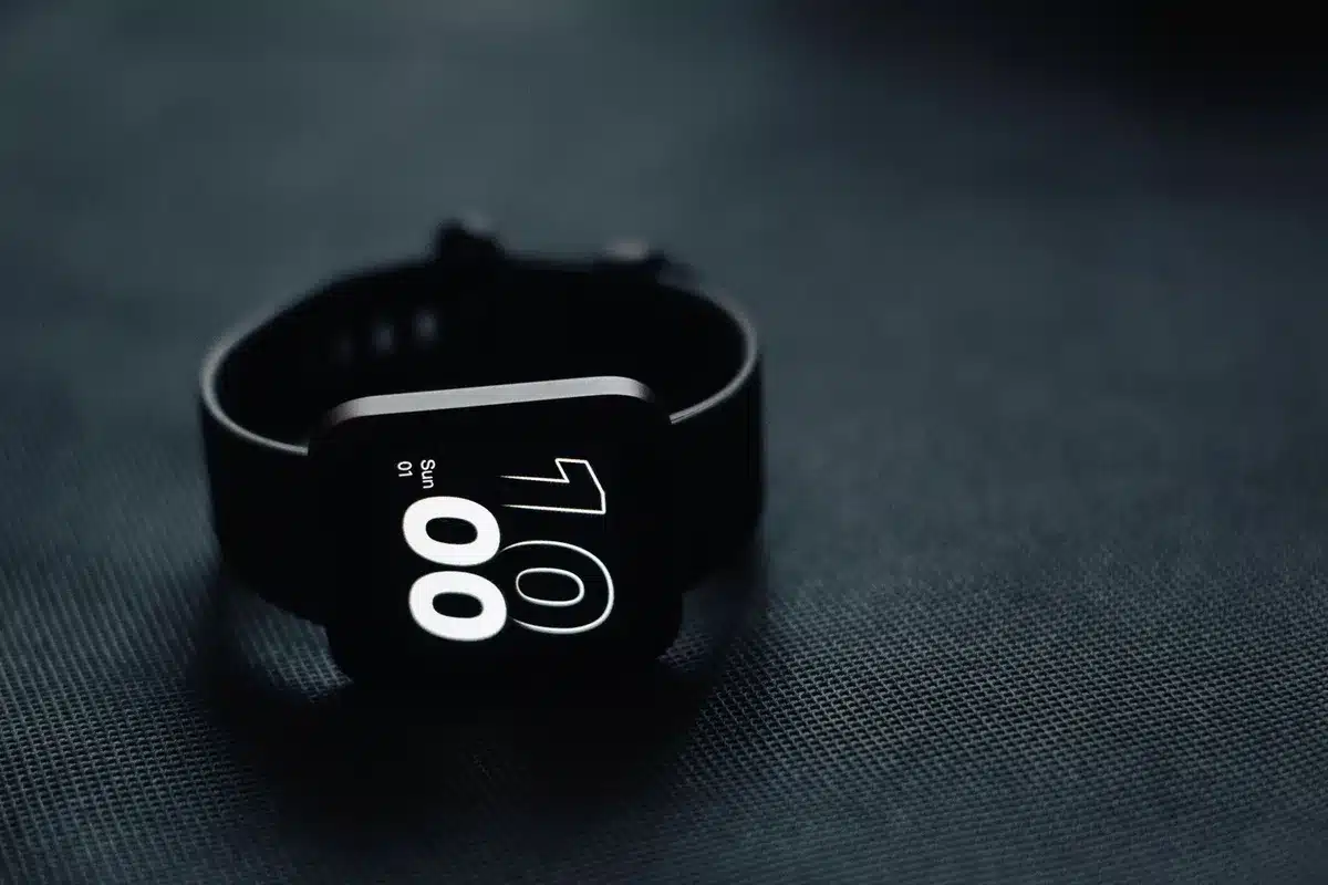 A clean retail display table with an anonymous smartwatch on a stand, price tags blurred and generic packaging around it