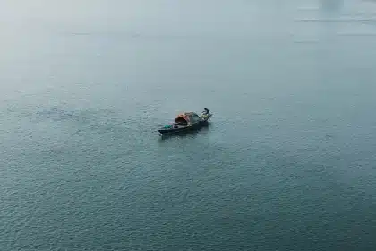 Línea de costa con valla fronteriza y embarcaciones anónimas al atardecer