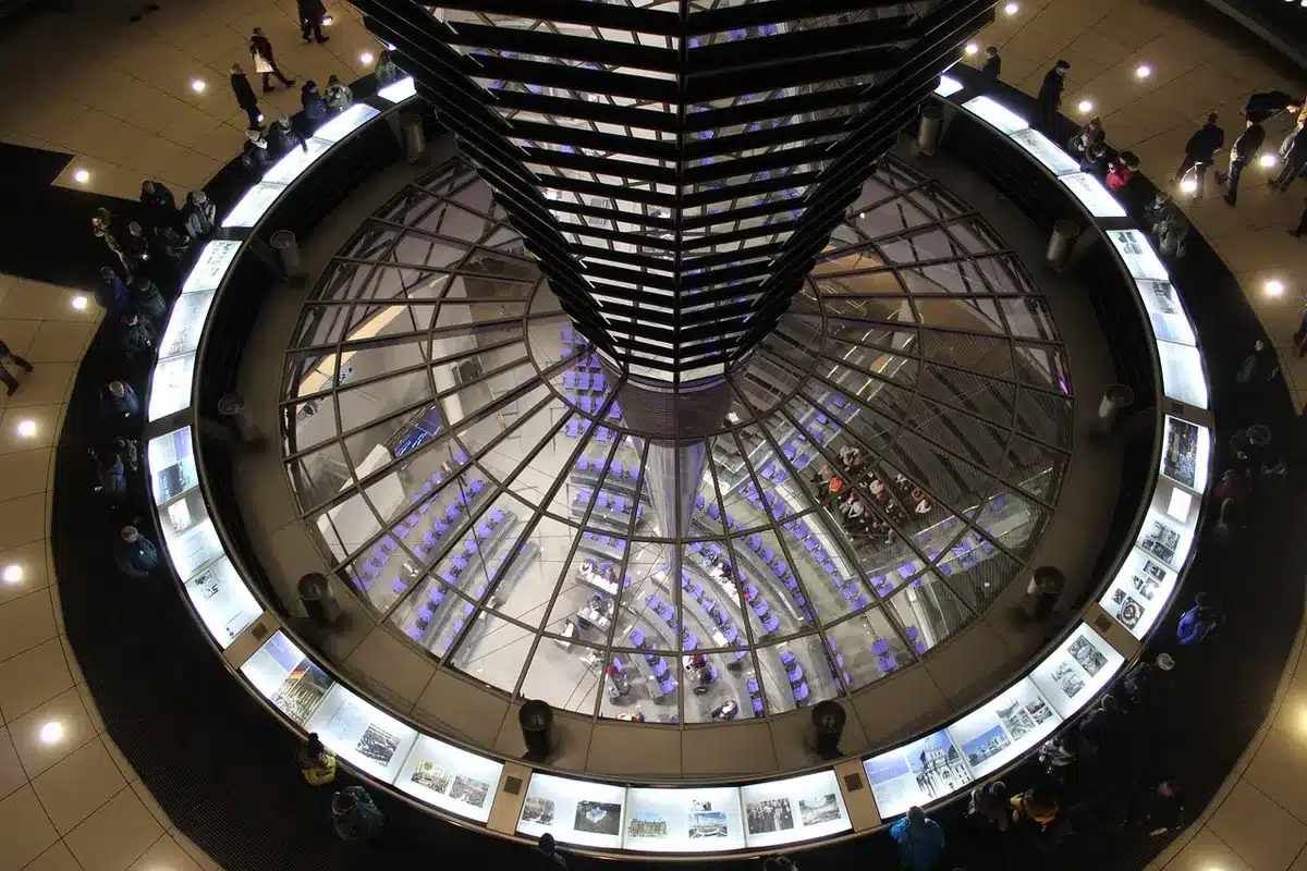 Wide night scene of an anonymous government building facade bathed in pale blue light, empty plaza in front, distant blurred silhouettes, no identifiable people or logos