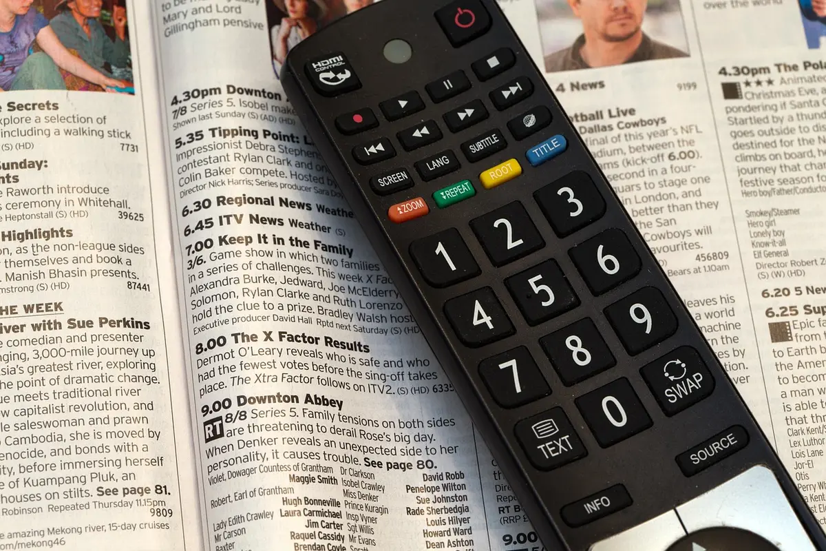 Close-up of a hand holding an anonymous remote control pointed at a blank TV, warm interior, no logos visible