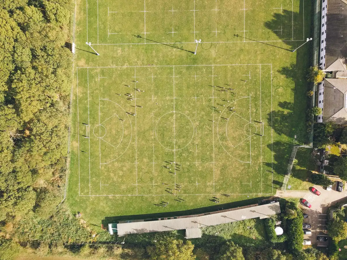 An empty training pitch at dawn with a single ball on the centre circle and a distant, anonymous stadium stand under soft morning light