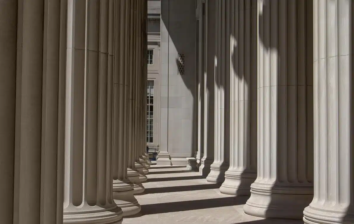 Long corridor in a palace with muted decorations, an empty red carpet runner and distant silhouettes, morning light