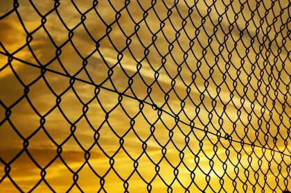 Línea costera con vallas y una barca vacía, mochilas y siluetas al fondo