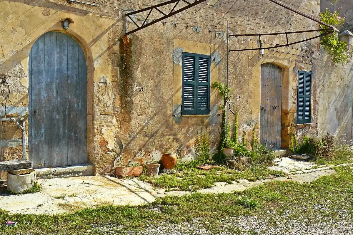 An empty stone street in a small abandoned Spanish village, old masonry houses and a distant lighting rig hinting at film activity