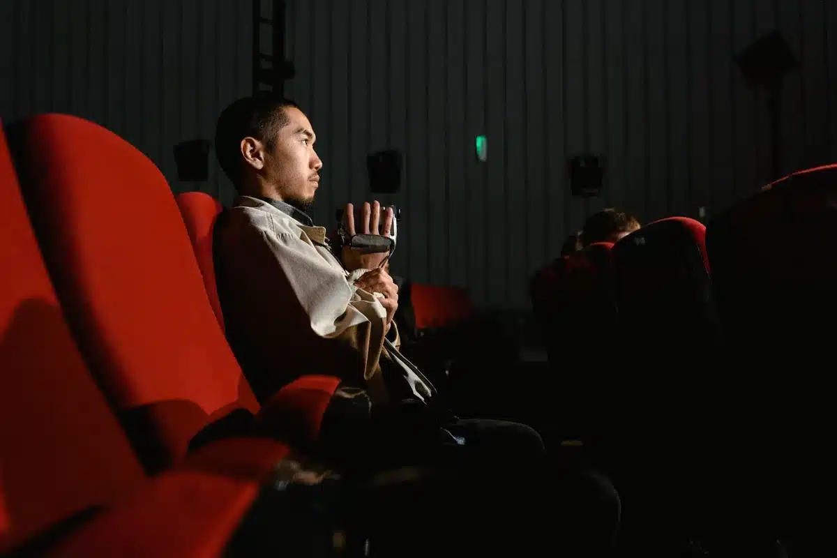 Anonymous crowd of TV viewers watching a large flat-screen displaying a reality-show promo, backs to camera, living room setting