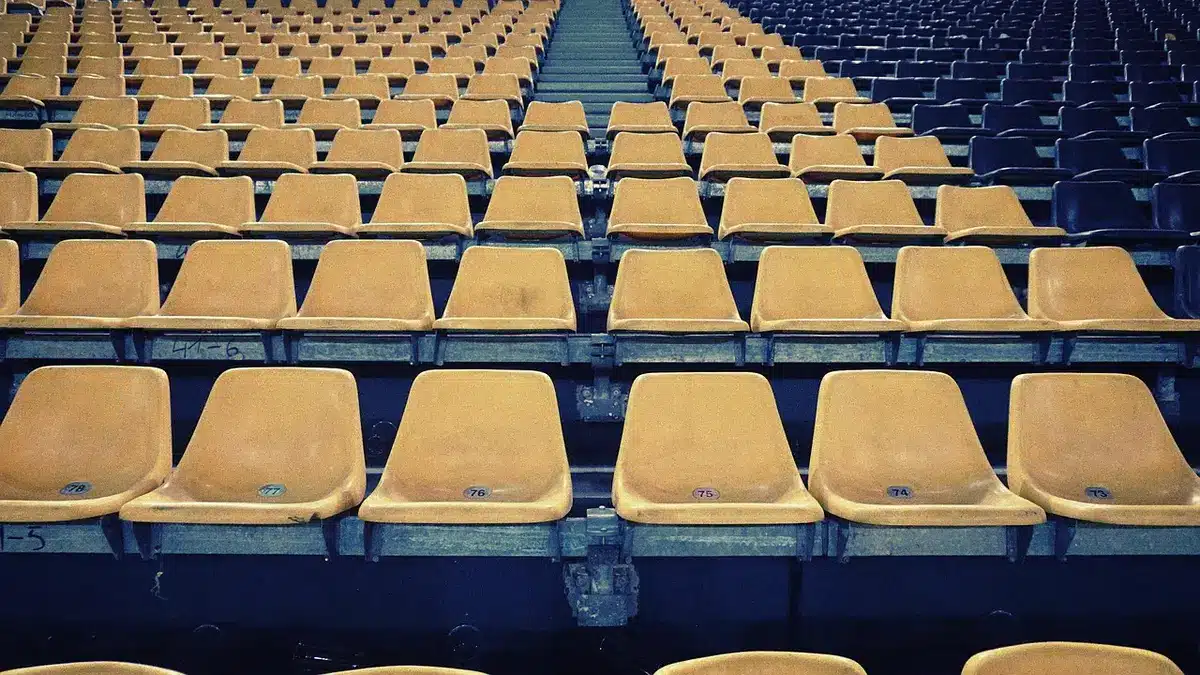 Empty stadium seats at dusk, a lone corner of the pitch under lights, no people