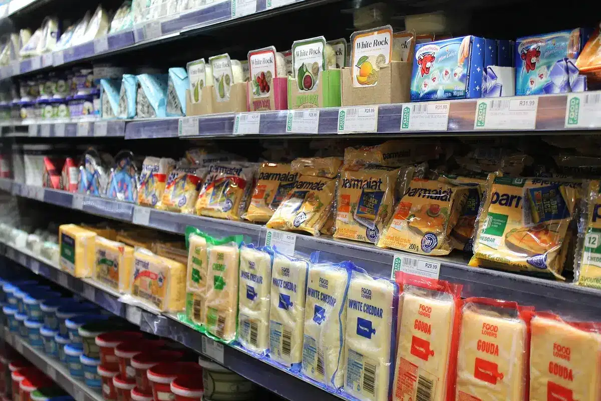 Empty supermarket aisle with stocked shelves and an anonymous shopping trolley in the foreground, soft daylight, quiet, inviting scene