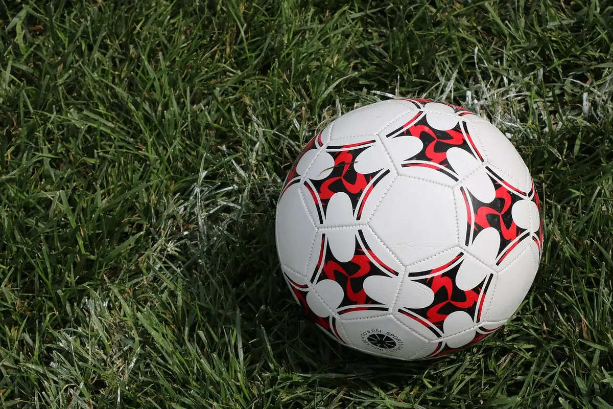Single soccer ball on an empty training pitch at dawn, distant stadium lights off