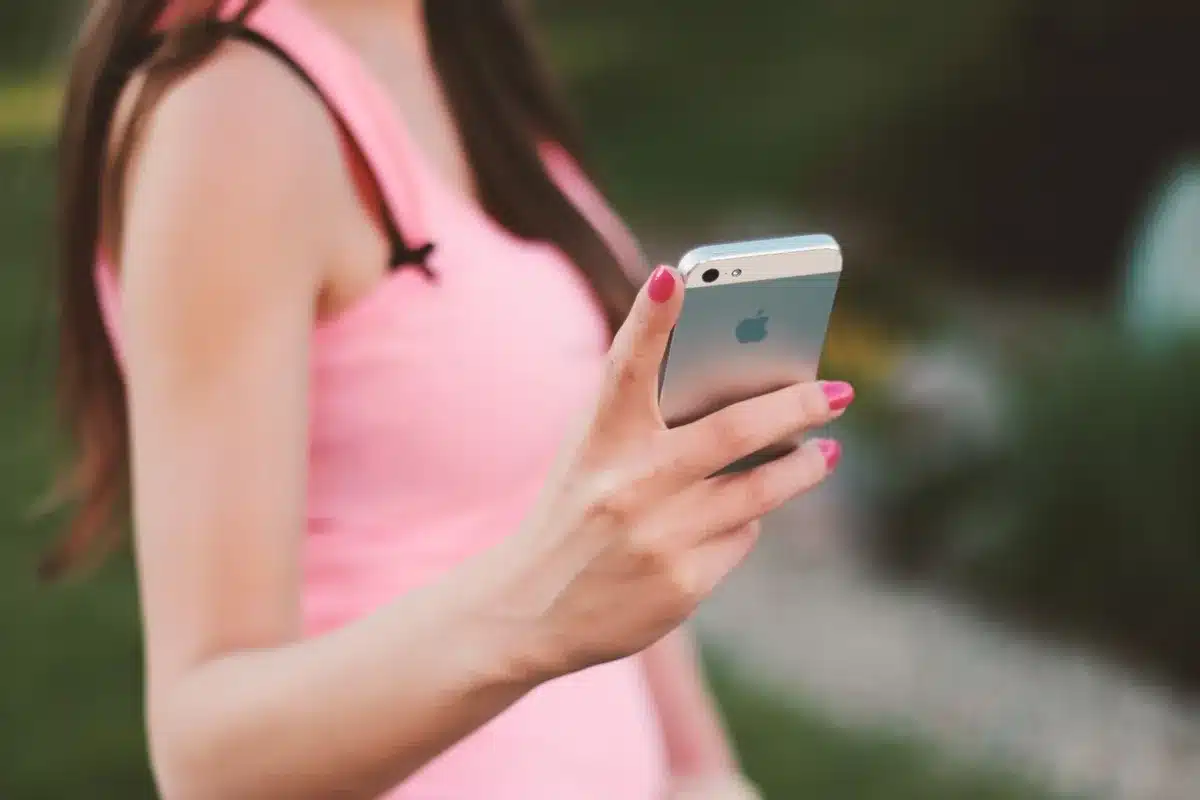 Close-up of an anonymous hand holding a blank-screen flagship phone against a shop countertop, blurred price tags in background, no brands visible