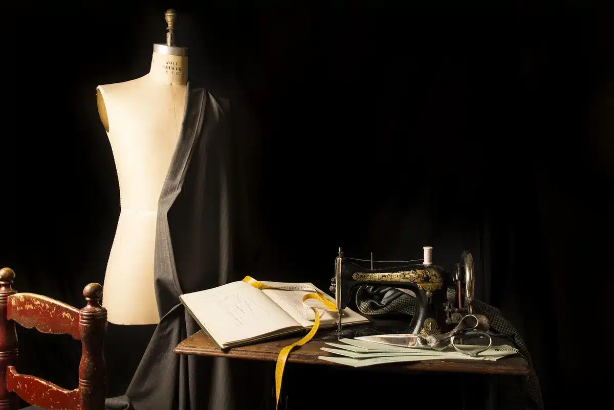 A quiet workbench strewn with swatches, measuring tape and unbranded suit jackets mid-construction, anonymous hands at work