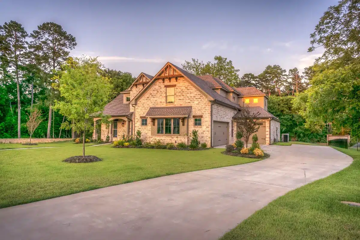 A modest suburban house exterior at dusk with warm light in the windows, an empty front path and a potted plant near the door, no identifiable features