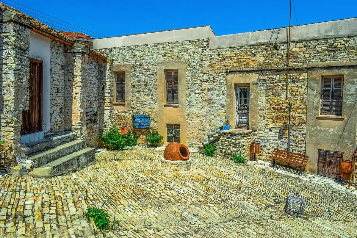 An empty village street with whitewashed facades and a rustic tiled square under soft morning light; no people visible, distant mountains on the horizon