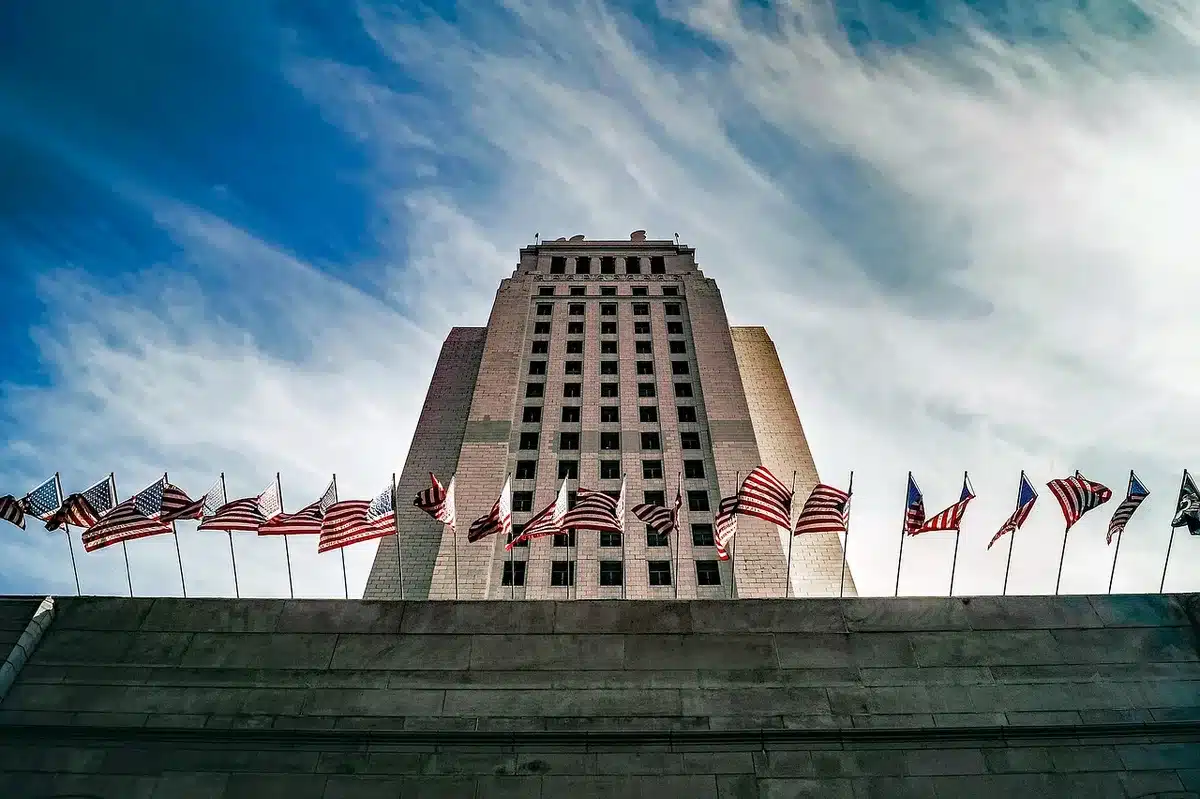 Wide shot of an anonymous historic government building facade adorned with rows of international flags, gentle crowd in the distance, Madrid-style square setting