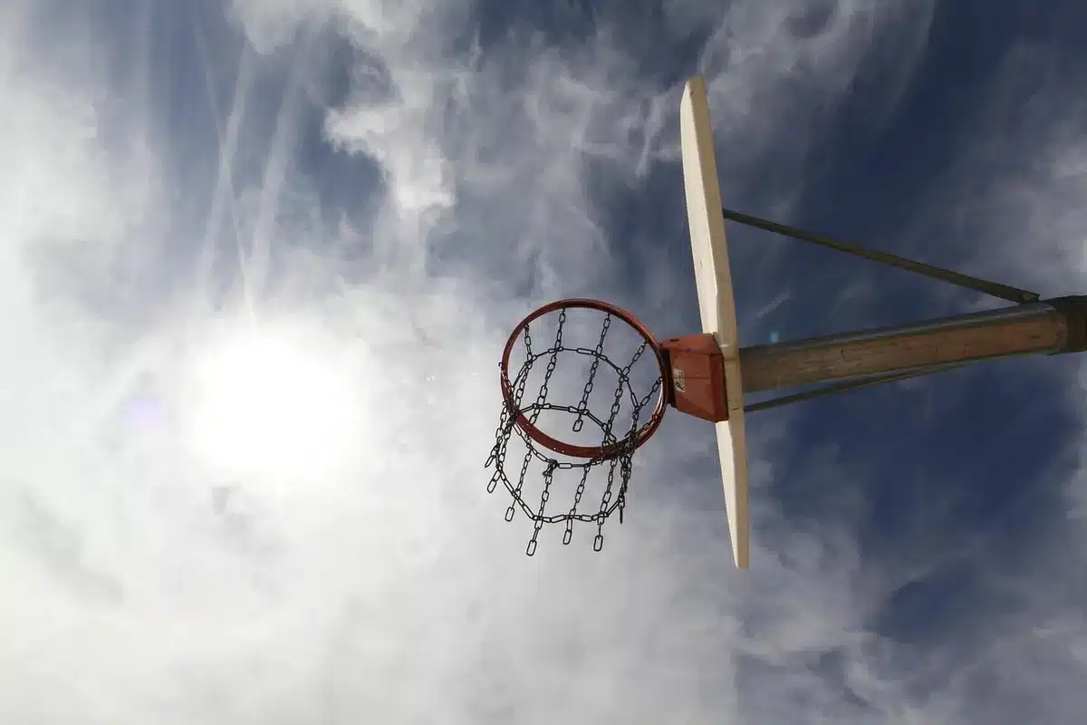 Empty arena with a basketball hoop and a lone ball on the court, subtle confetti traces, no people visible