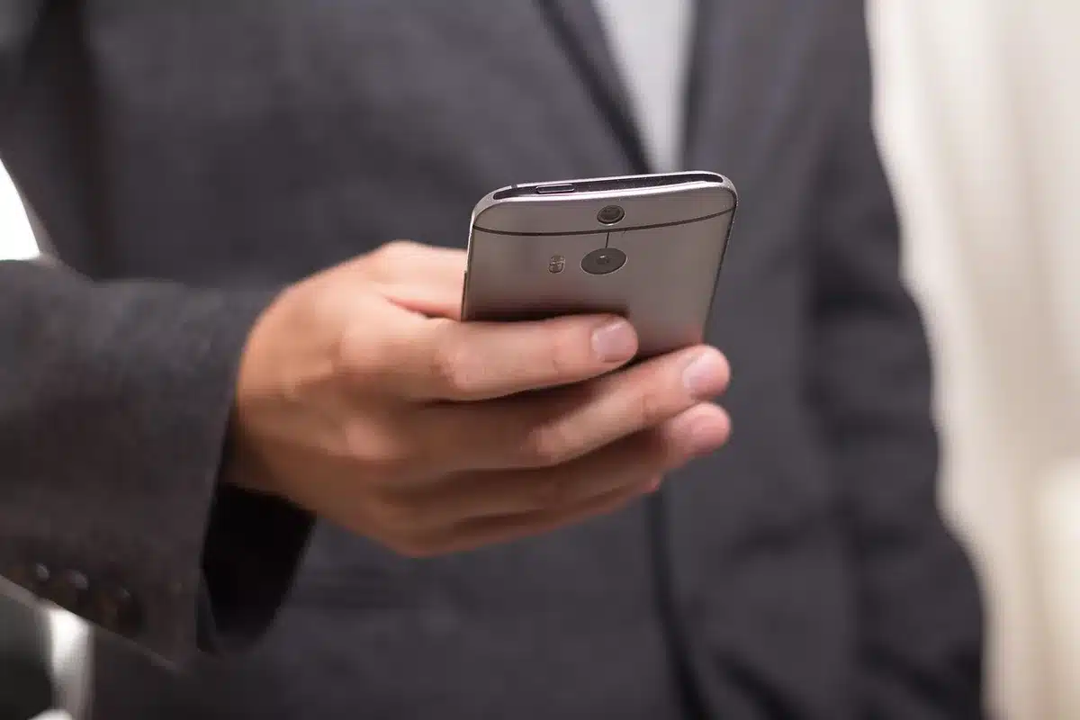 A close-up of a mobile phone on a kitchen table with a blurred voice memo app open, an anonymous pair of hands resting nearby, domestic scene implying a private call