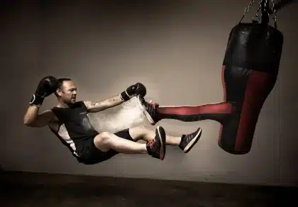 Manos anónimas agarrando la cuerda de un ring de boxeo con un póster desgastado al fondo