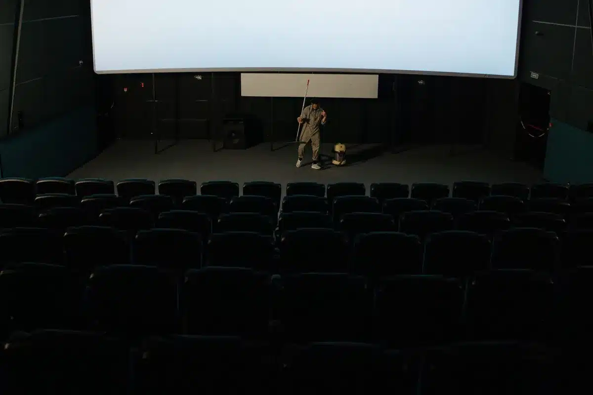 Empty outdoor stage with a single unbranded guitar on a stand under warm spotlight, empty seats in soft focus