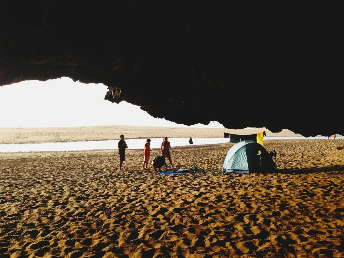 A small beach camp with two overturned bowls and footprints in sand, empty but suggesting recent activity and dispute